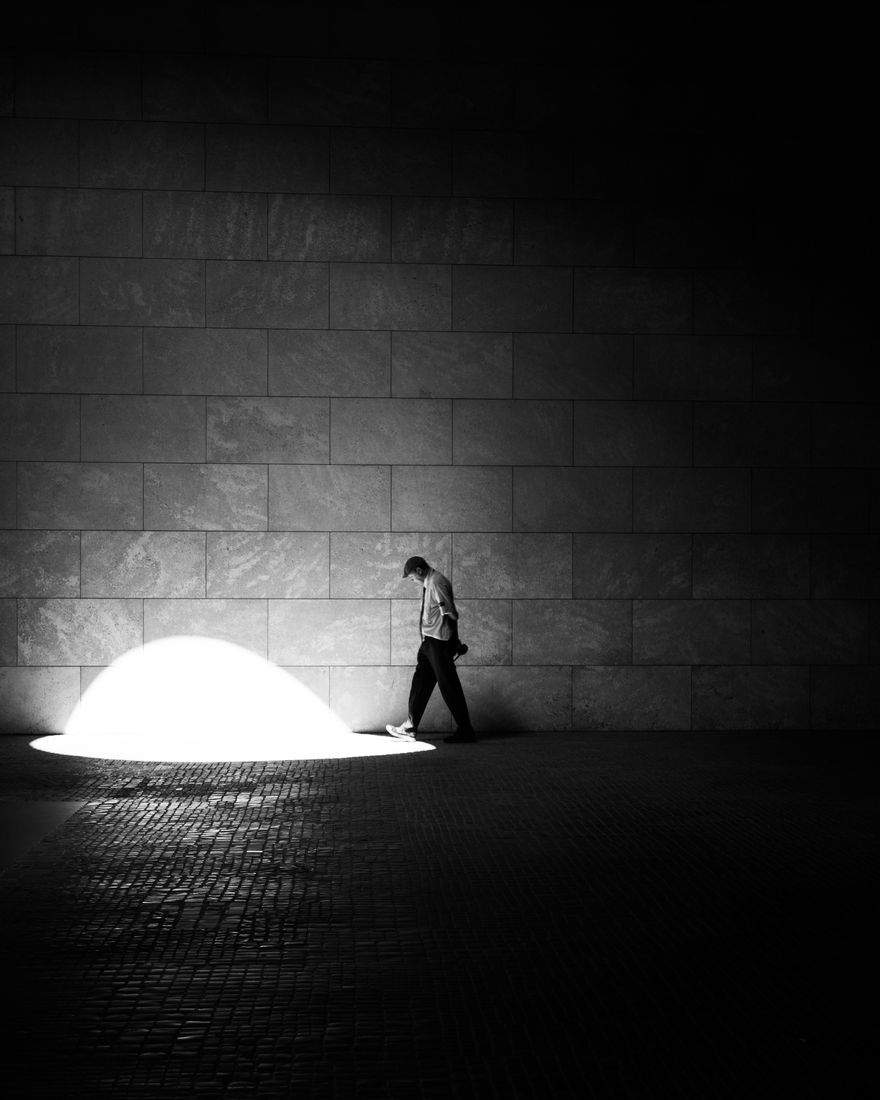 A man walks along a stone wall at the edge of a bright dome of light on the pavement