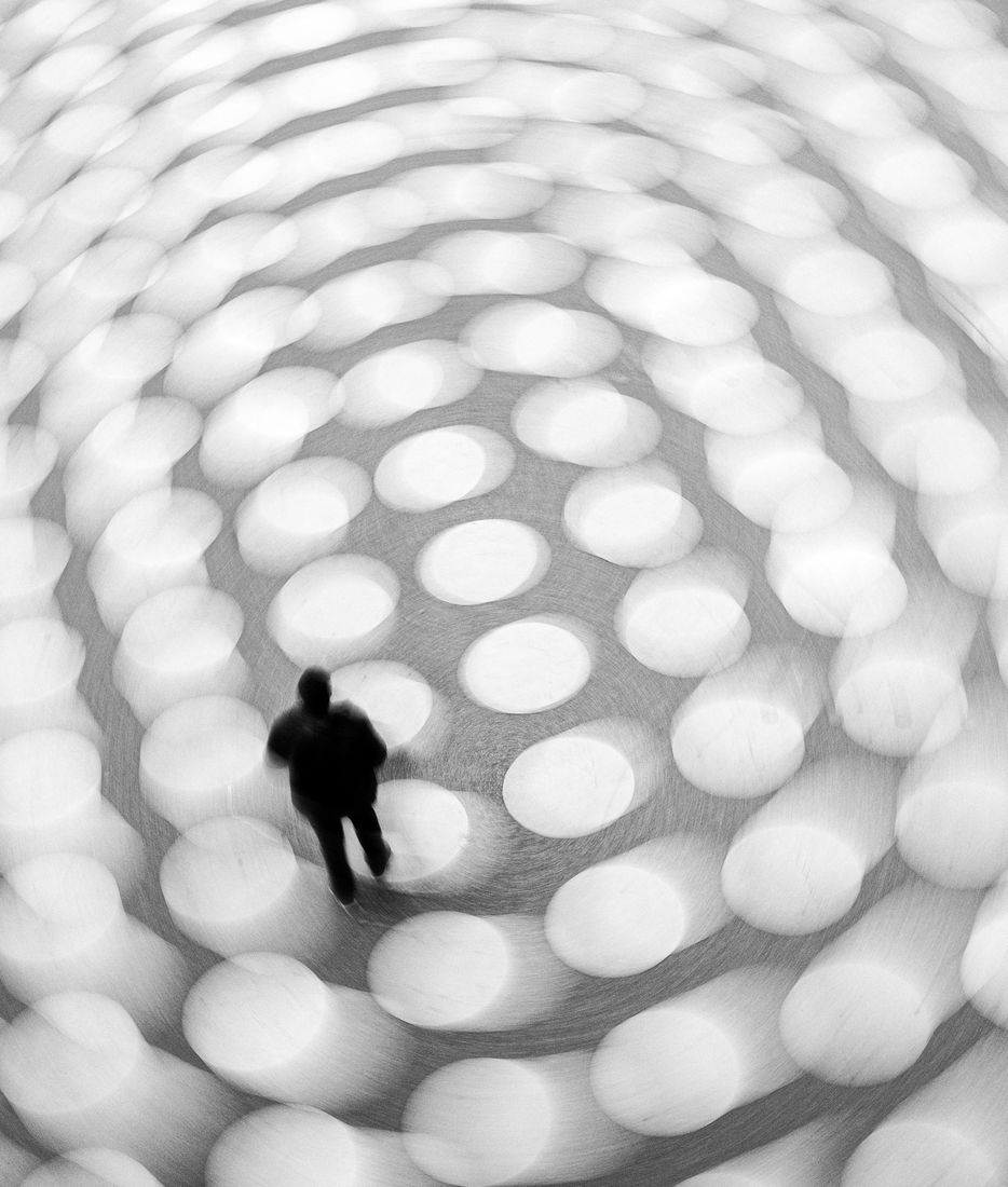Seen from above, a lone figure crosses a floor of blurred white discs spiralling outwards