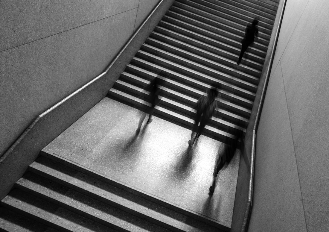 Blurred figures climb a wide stone staircase, their shadows stretched across the landing
