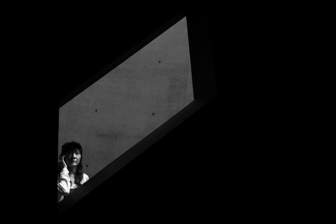 A woman looks out from a slanted opening in a dark concrete wall